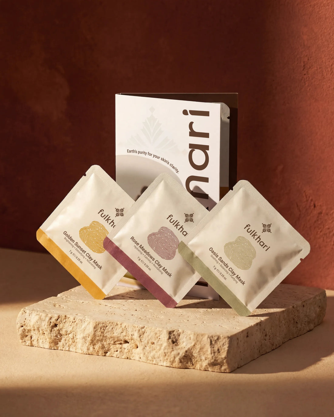Fulkhari Fuller's Earth Clay Mask Trio Sampler set featuring Golden Sunset, Rose Meadows, and Oasis Sands sachets on travertine stone.