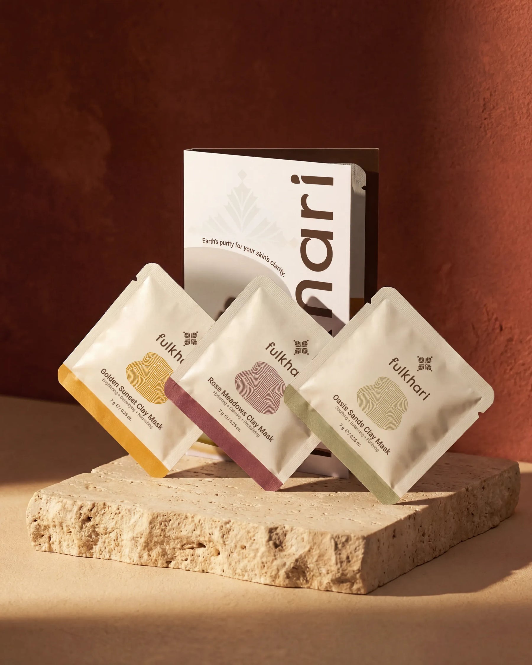 Fulkhari Fuller's Earth Clay Mask Trio Sampler set featuring Golden Sunset, Rose Meadows, and Oasis Sands sachets on travertine stone.