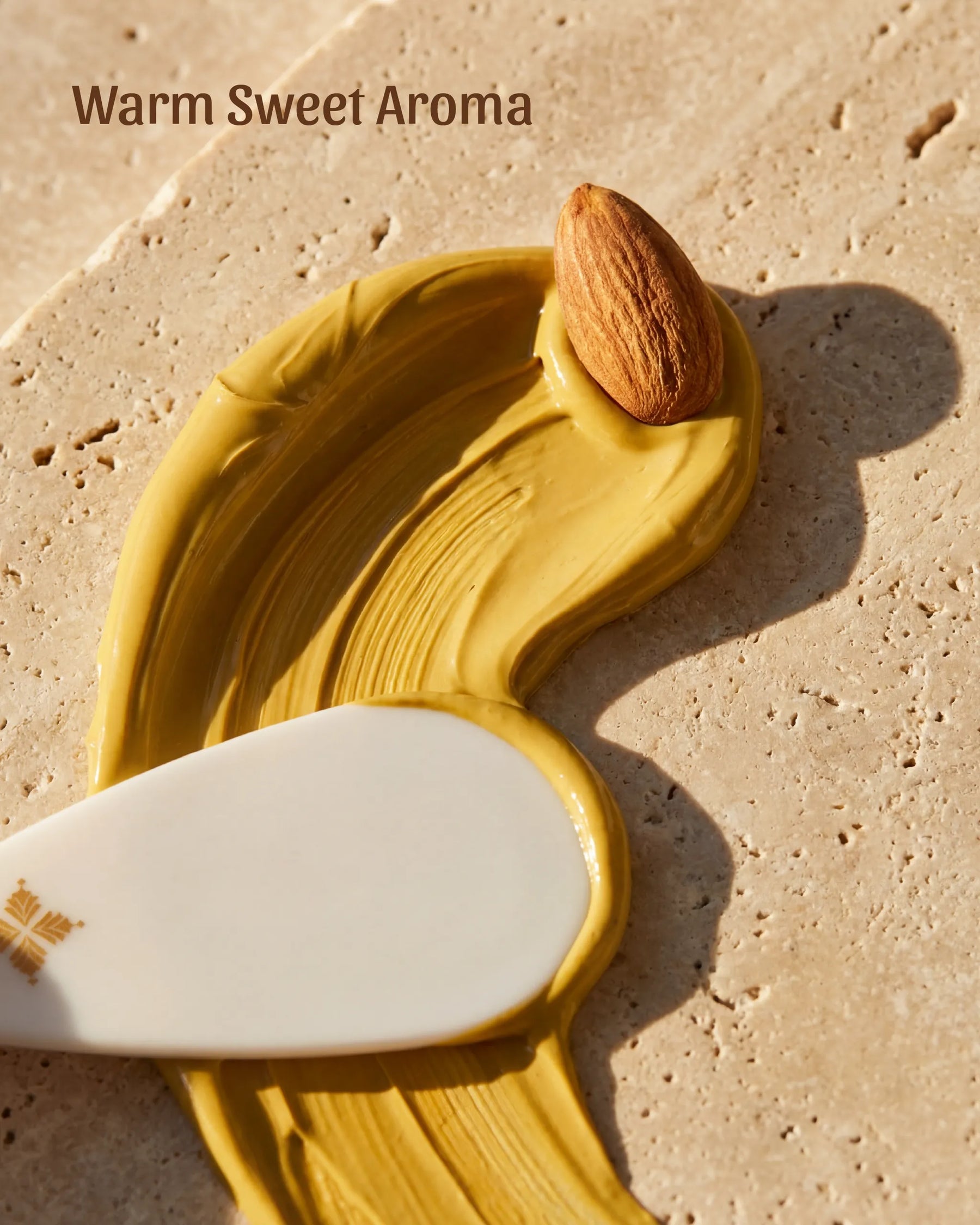 Smooth, buttery smear of yellow Fuller's Earth clay mask with a raw almond on beige stone.