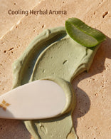 Whipped, cooling smear of sage green Fuller's Earth clay with a chamomile flower on stone.