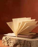 Open booklet of Fulkhari blotting papers with translucent sheets fanned out on stone, showing the delicate, oil-absorbing texture.