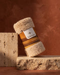 Fulkhari TerraPlush Face Towel tightly rolled on beige travertine stone, an ultra-soft reusable makeup remover cloth in warm oatmeal beige.